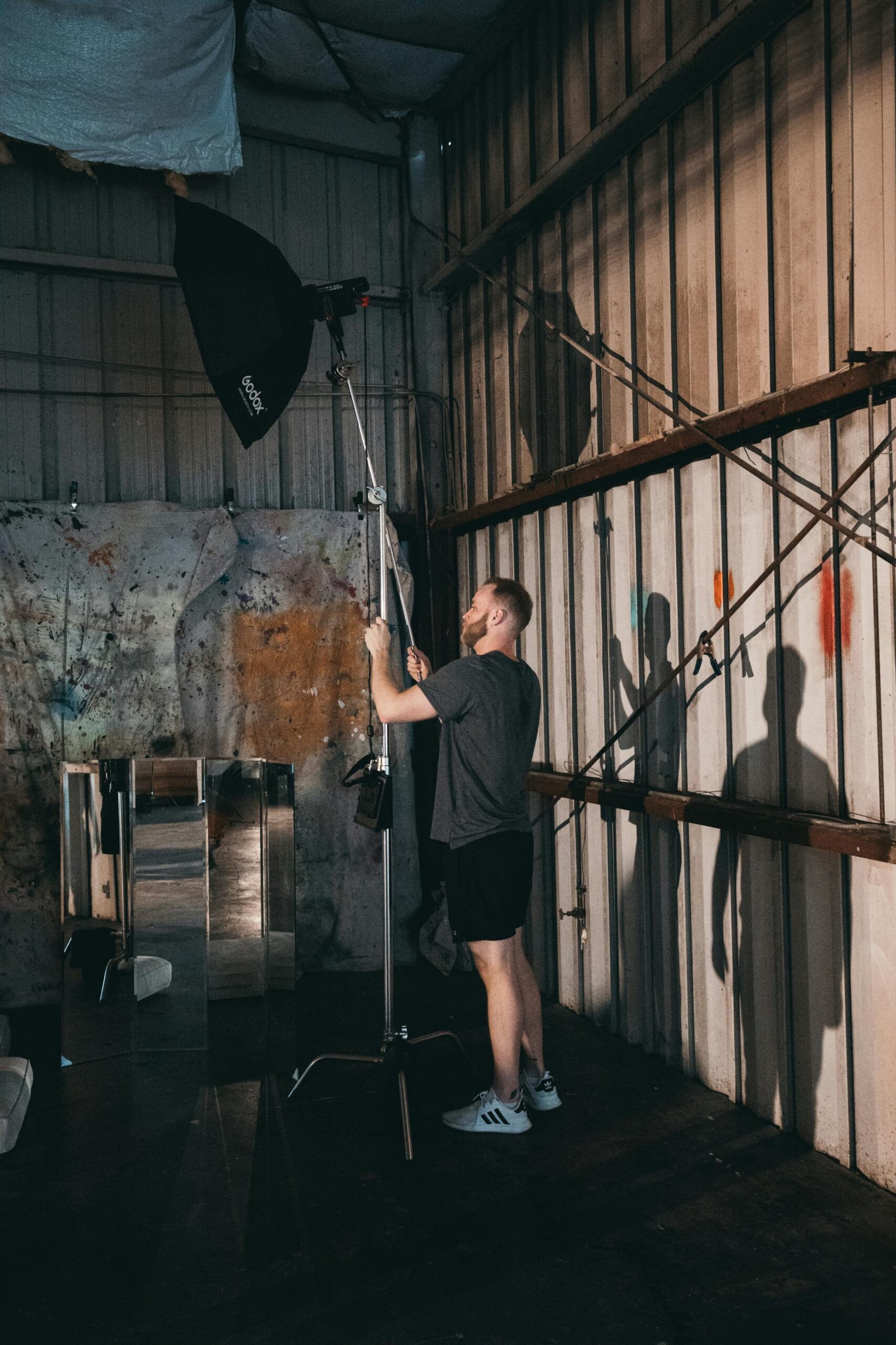 A man adjusts lighting equipment inside an industrial-style film set.